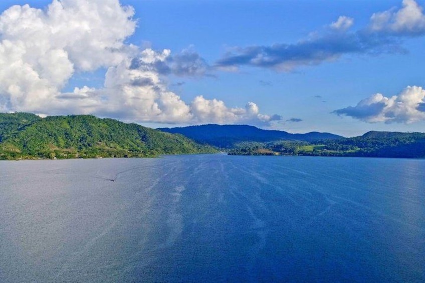 A calm lake with a clear horizon, surrounded by green hills and a partly cloudy sky. 3