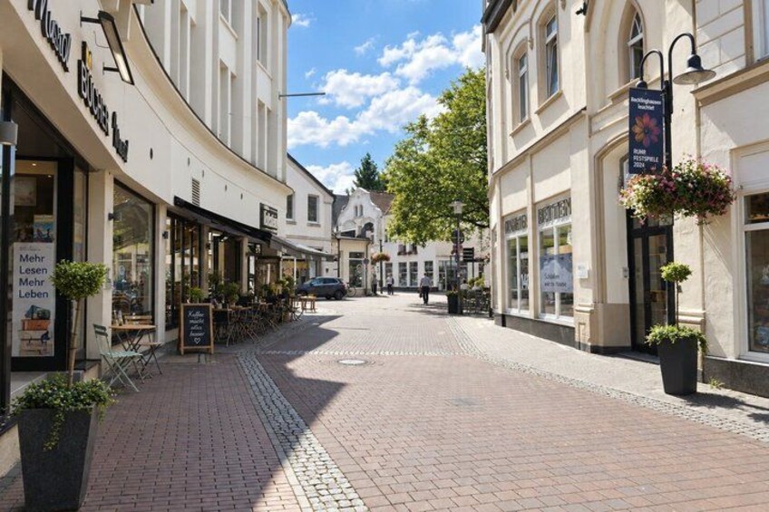 A cobblestone street lined with cafes and shops, a clear sky, and a few pedestrians. 2