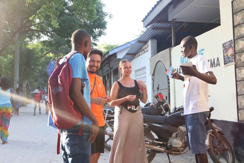 A group of people standing outdoors, a motorcycle, and a building with a sign. 2