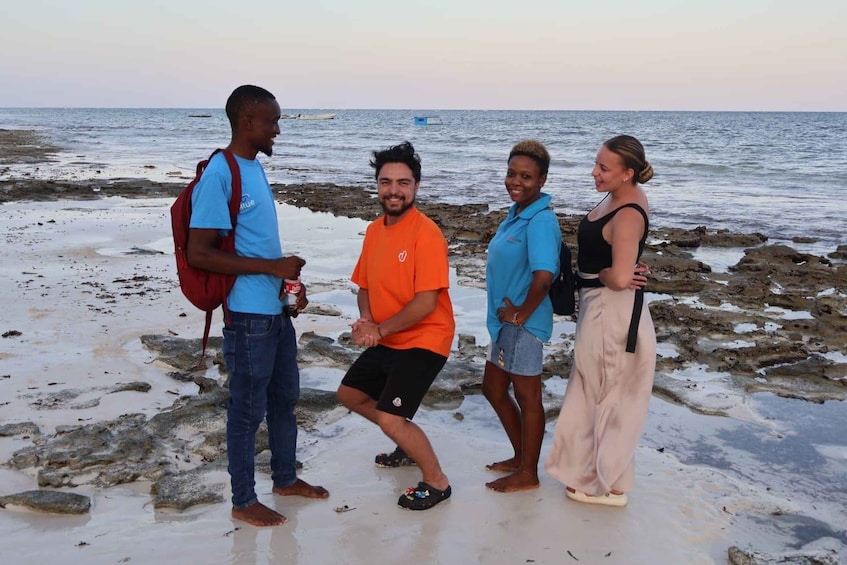 A group of people standing on a rocky beach with the ocean in the background. 4