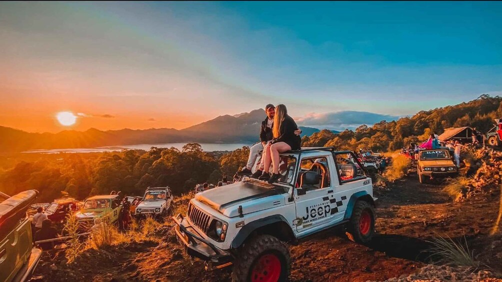 En Jeep med et par på taget, solnedgang og et bjergrigt landskab. 5