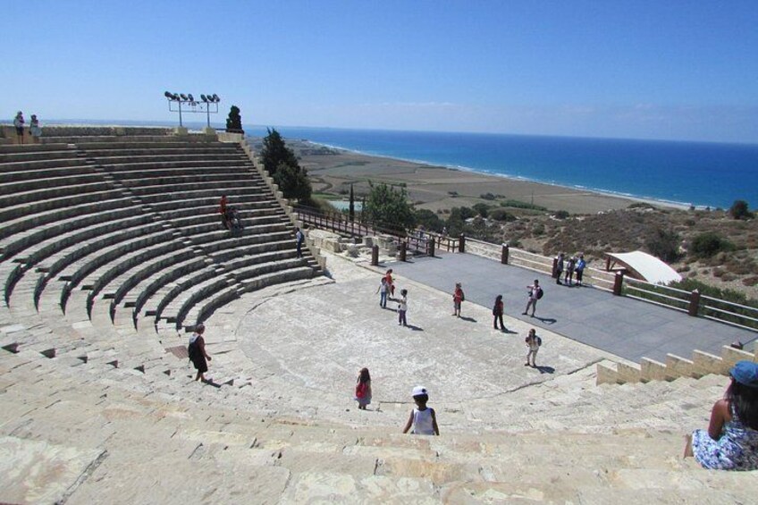 An ancient amphitheater with stone steps and a stage, overlooking a coastal landscape. 4
