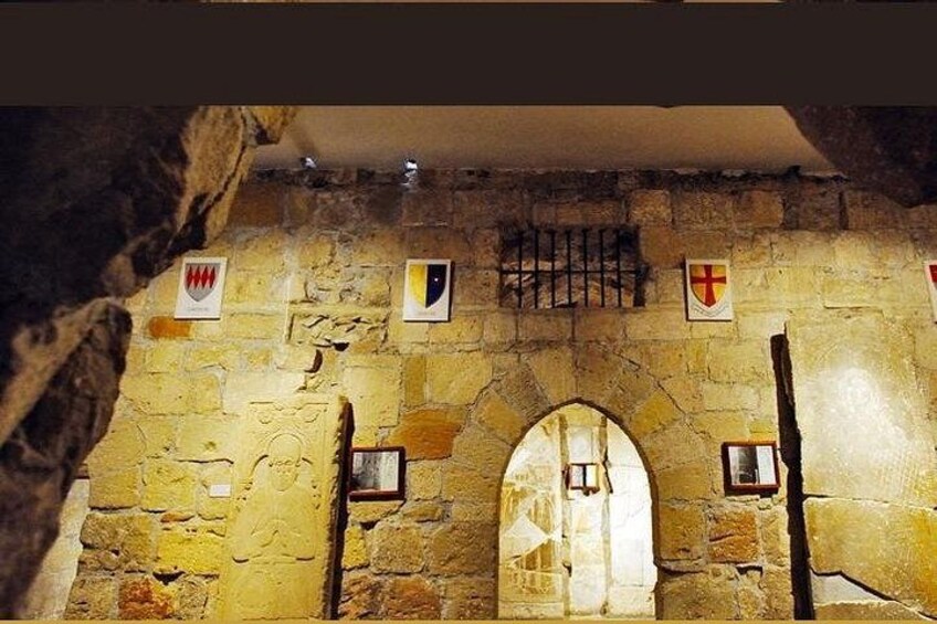 A stone wall with a medieval archway, banners, and a barred window. 2