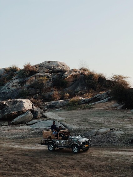 A jeep with passengers driving on a dirt road surrounded by large rocks and sparse vegetation. 4