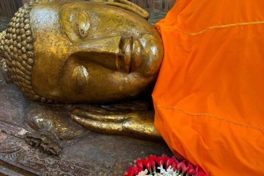 A golden Buddha statue with intricate carvings, a person in orange robes, and a red and white flower arrangement. 2