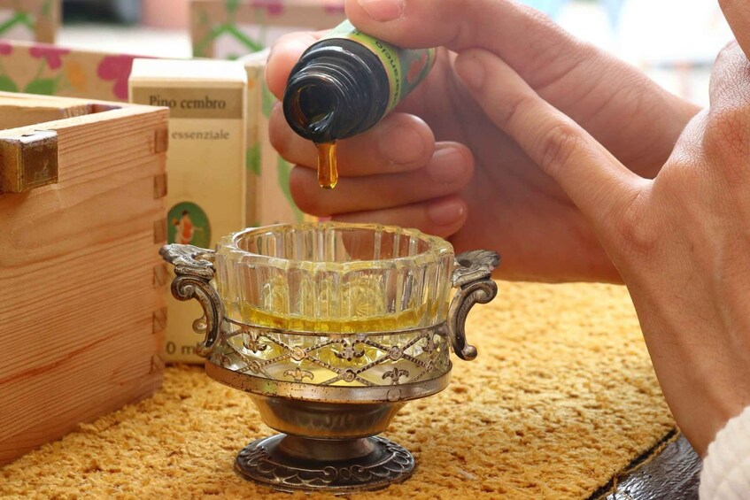 A hand pouring a yellow liquid from a bottle into a glass container with ornate handles. 5
