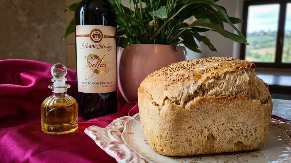 A loaf of bread, a bottle of wine, and a small bottle of oil on a table with a red cloth. 1