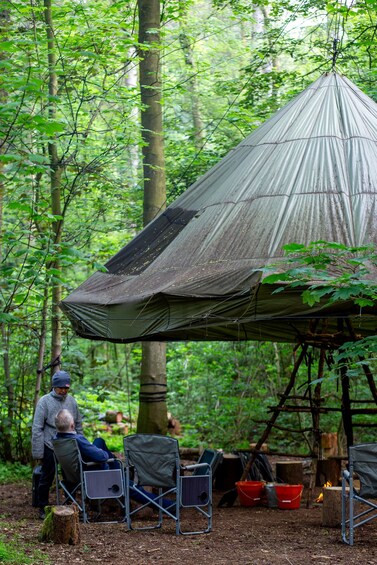 A forest with a large, dome-shaped tent and two people sitting on chairs. 4