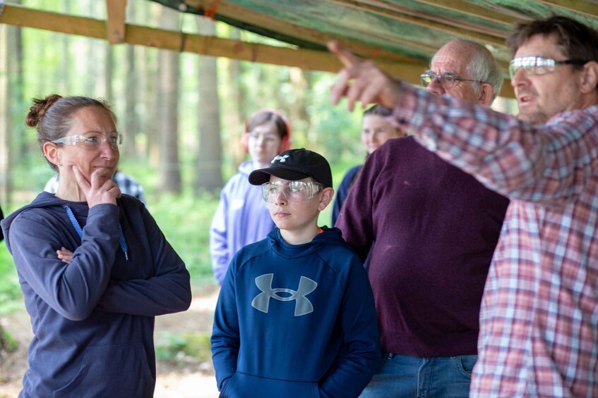 A group of people outdoors, some wearing safety goggles, under a wooden shelter. 5