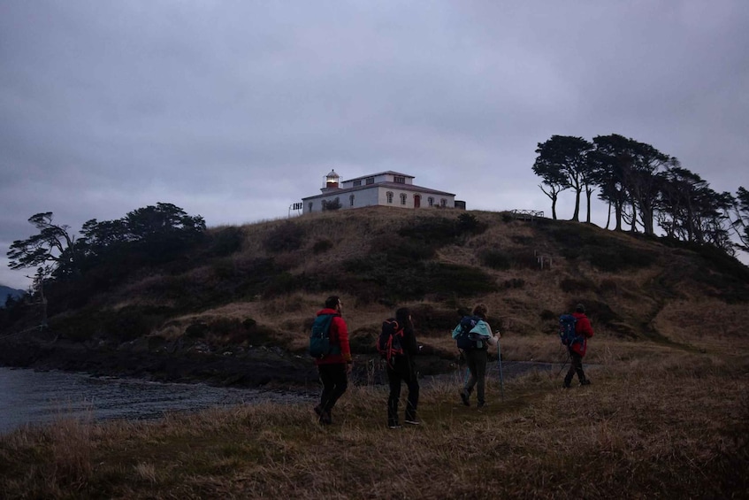 Eine Gruppe Wanderer auf einer grasbewachsenen Hügel mit einem Leuchtturm im Hintergrund. 5