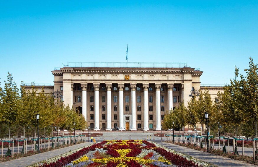A large neoclassical building with columns, a flagpole, and a flower bed in the foreground. 2