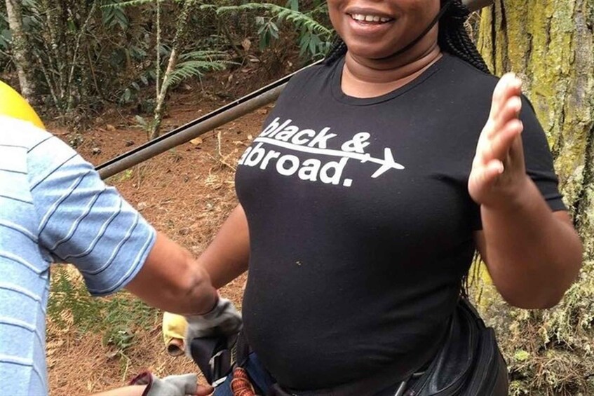 Una persona con una maglietta nera con la scritta 'black & abroad', che tiene un bastone da passeggio e si trova in una zona boschiva. 4