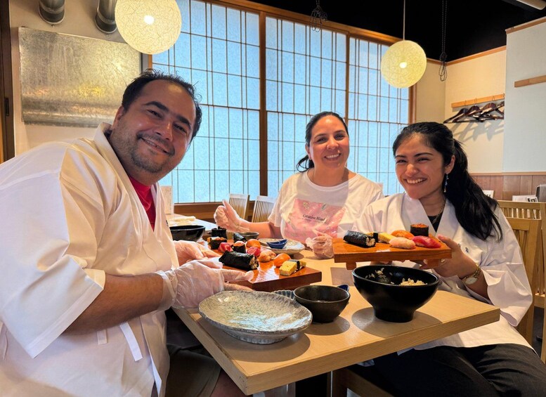 Three people in a kitchen setting with sushi on the table. 1