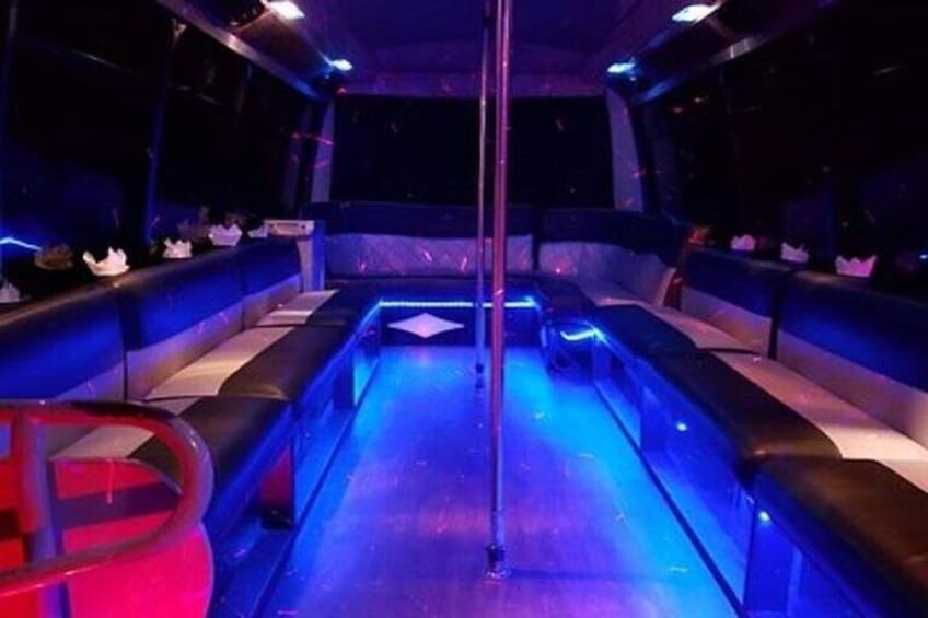 A dimly lit room with blue lighting, a central pole, and seating along the walls. 3