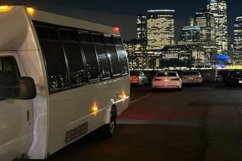 A white bus parked in a lot with a city skyline in the background. 2