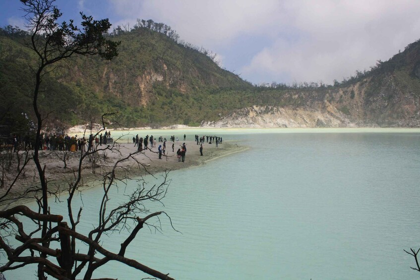 A group of people gathered by a calm turquoise lake, surrounded by forested hills. 5