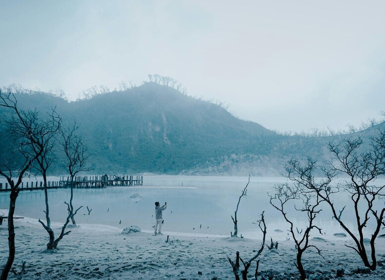 A snowy landscape with a person taking a photo, a frozen lake, and leafless trees. 1