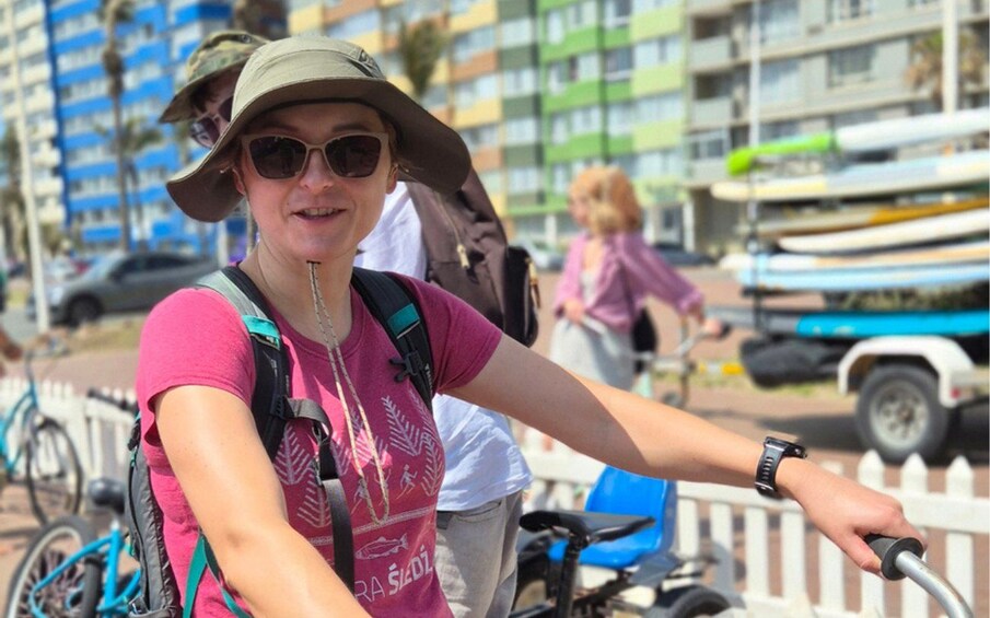 A person on a bicycle with a backpack, a white fence, and boats in the background. 5