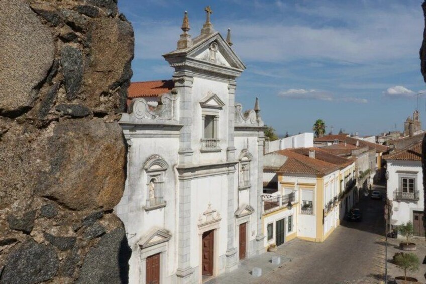 A historic church with a bell tower, a cobblestone street, and traditional buildings. 1