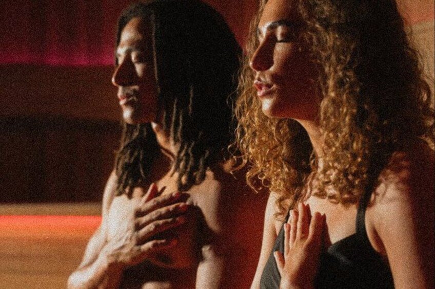 Two people sitting closely together, one with long hair and the other with curly hair, in a dimly lit indoor setting. 1