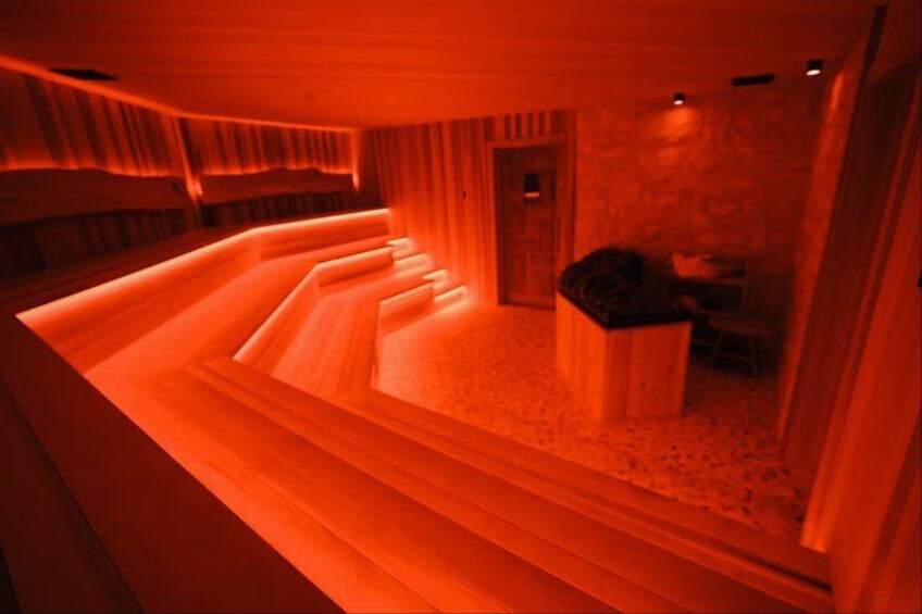 A red-lit spa with wooden benches and a stone wall. 4