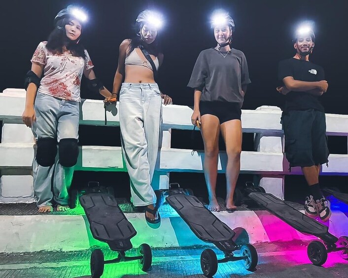 Four people standing on a platform with skateboards, wearing protective gear, and holding lights. 1
