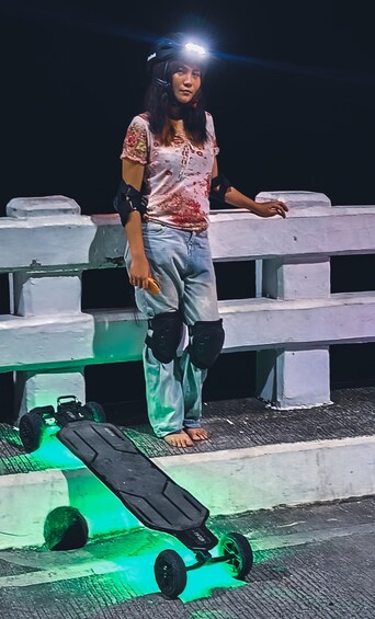 A person standing on a skateboard with a headlight, wearing protective gear, and holding a phone. 4