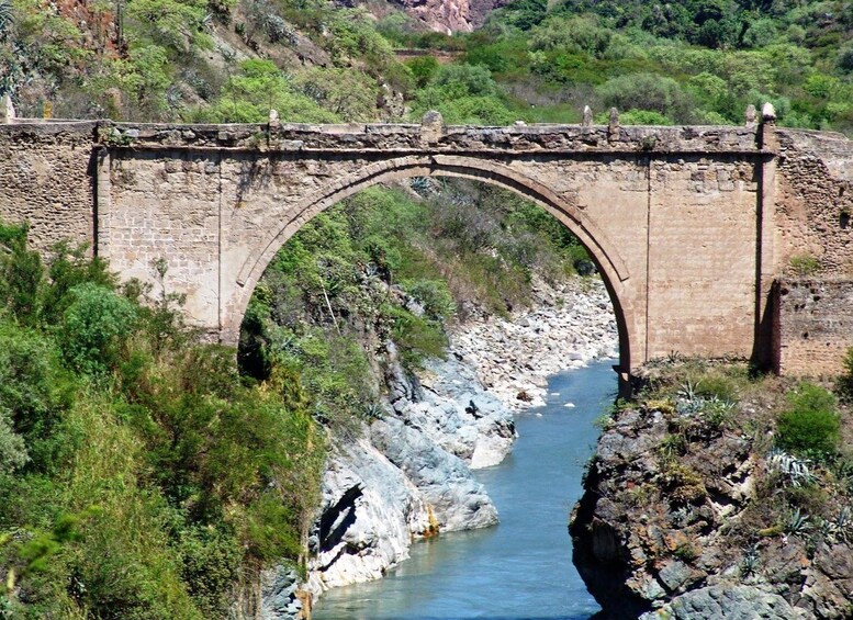 An arched stone bridge over a river with rocky banks and greenery. 1