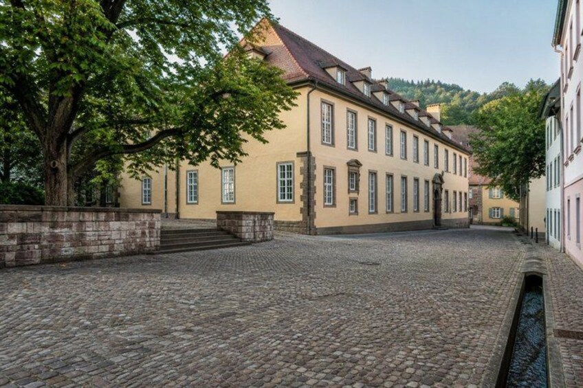 A cobblestone street, a large building with a red roof, and a tree. 2
