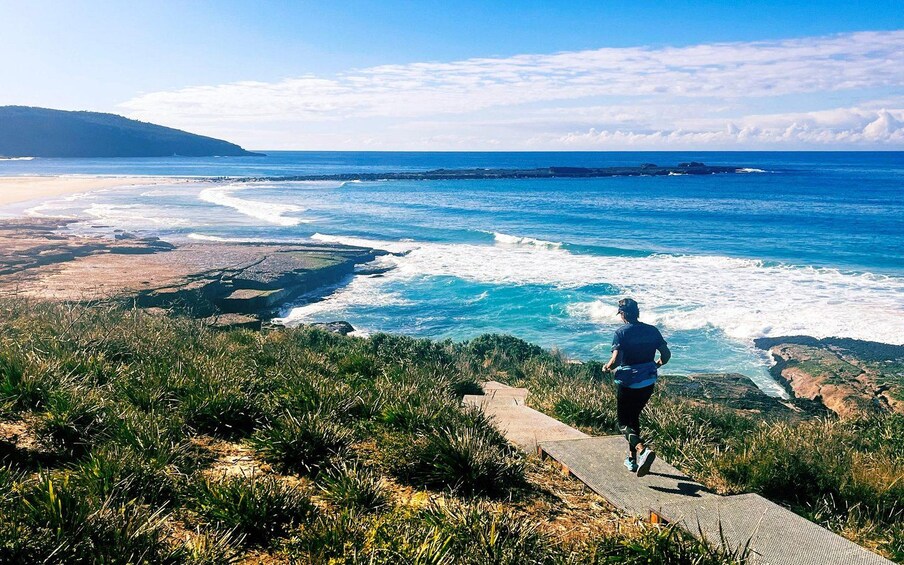 Una persona trotando por un sendero costero con olas del océano al fondo. 1