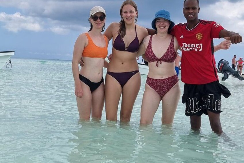 Four people standing in shallow water with a boat and a clear sky in the background. 2