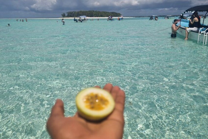 A hand holding a half-cut fruit, a tropical beach with clear turquoise water, and people in the distance. 3