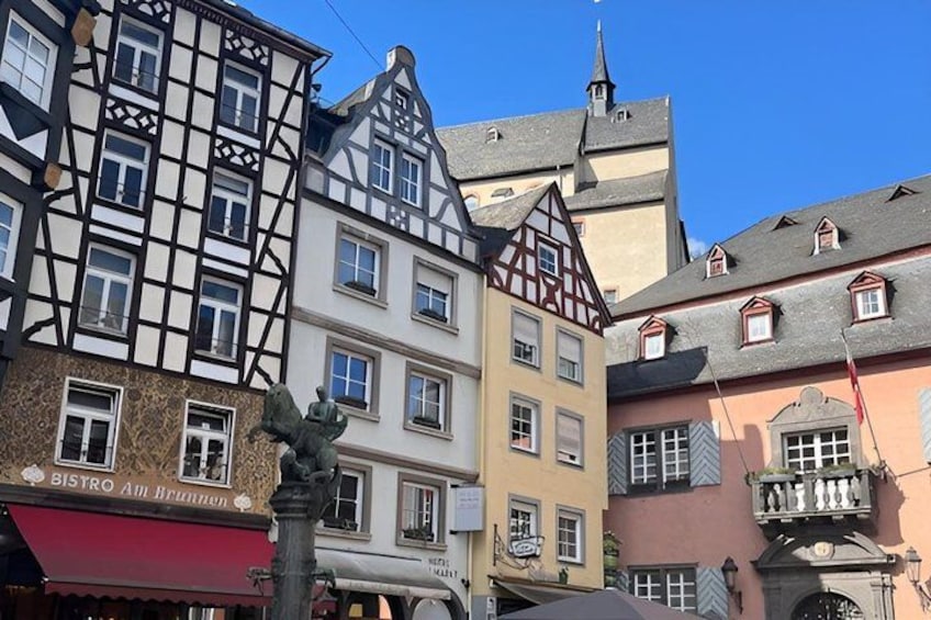 A street with traditional half-timbered buildings, a bistro, and a statue. 1