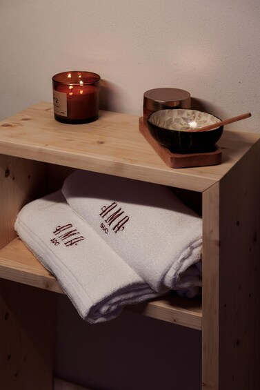 A wooden shelf with a lit candle, a bowl, and folded towels. 4