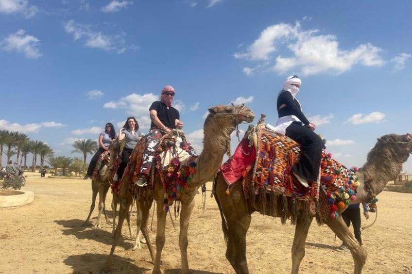 A group of people riding camels in a desert landscape with palm trees and a clear sky. 2