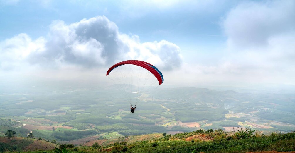 A paraglider over a hilly landscape with fields and a cloudy sky. 5
