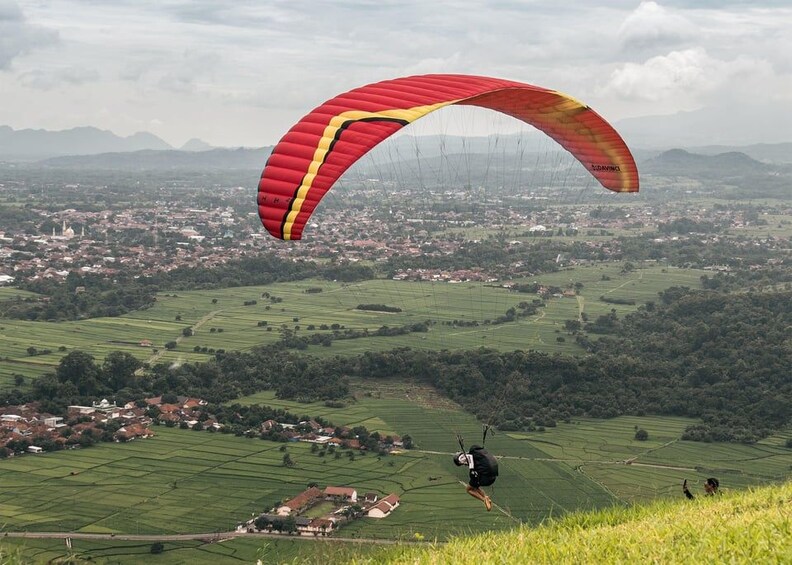 A person paragliding over a rural landscape with fields and a distant town. 1