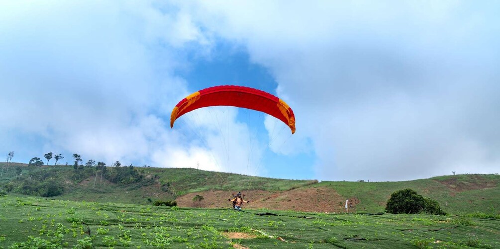 A person paragliding over a green field with a red and yellow parachute. 3