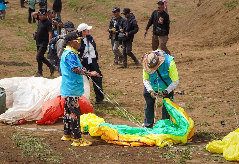 People preparing a large parachute on a dirt ground. 4