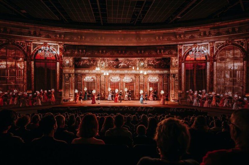 A theater with ornate architecture, a stage, and an audience. 2