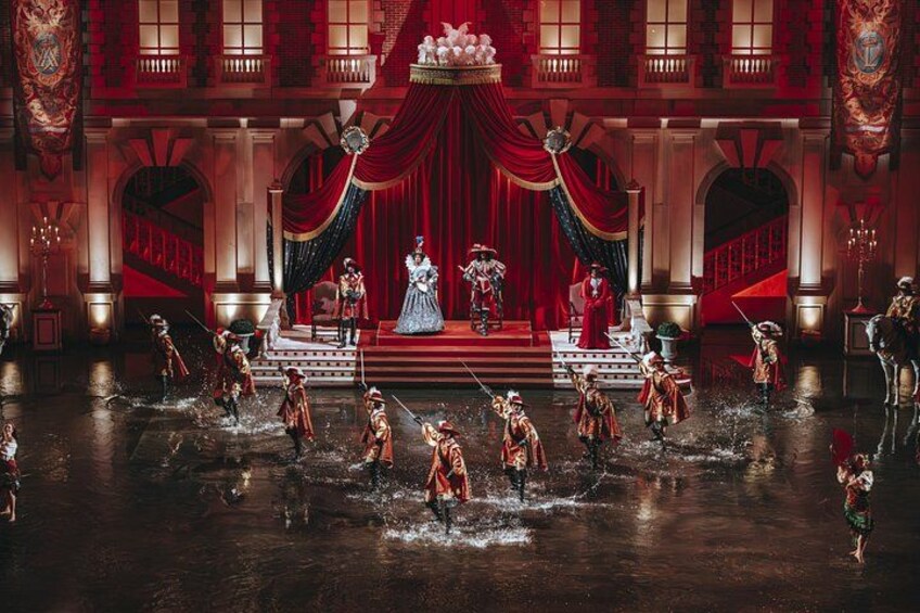 A theater stage with actors in period costumes, a grand staircase, and a large chandelier. 4