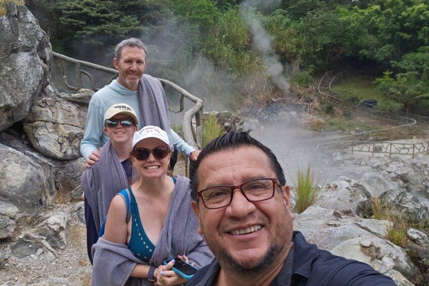 A group of people standing near a hot spring with steam rising from the water. 1