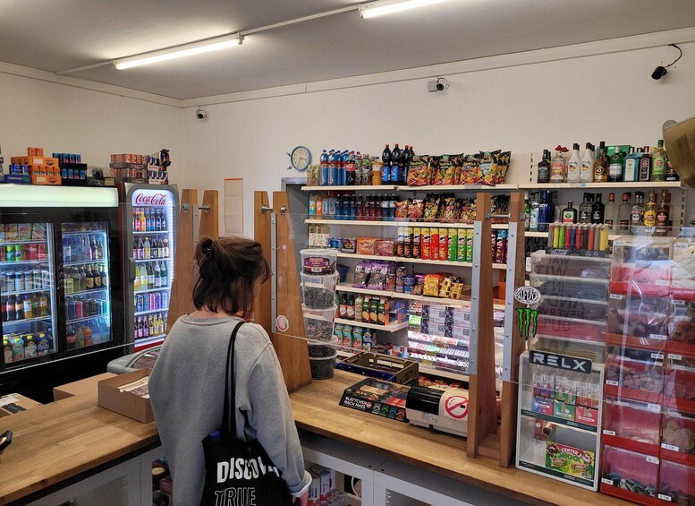 A person in a store aisle with shelves stocked with snacks, beverages, and other items. 4