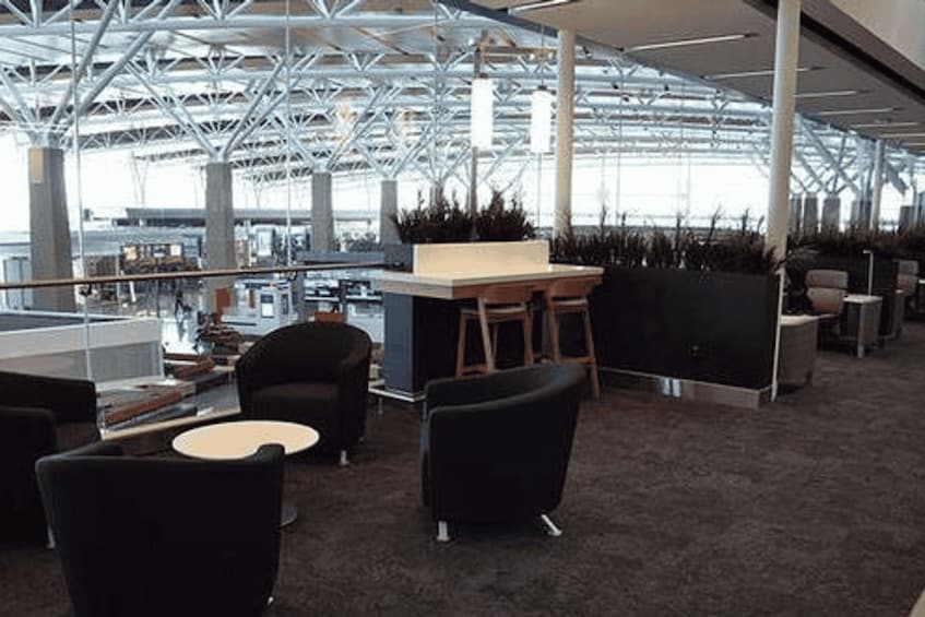 An office space with modern furniture, a high ceiling with a metal framework, and large windows allowing natural light. 5