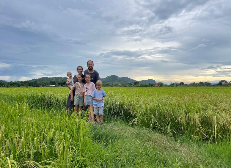 Une famille se tient dans un champ d’herbe haute, sous un ciel nuageux, avec des montagnes en arrière-plan. 4