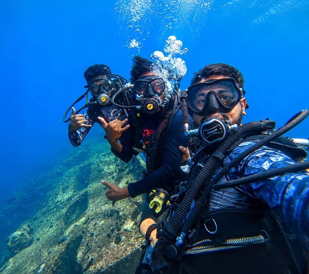 Three scuba divers underwater with their gear, surrounded by clear blue water and rocky ocean floor. 5