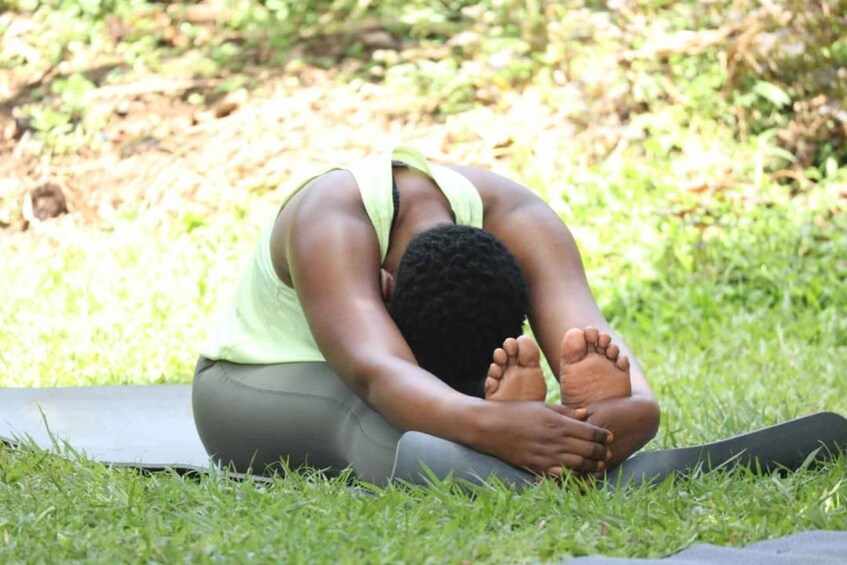 A person in a green tank top and gray leggings performing a yoga pose on a mat outdoors. 3