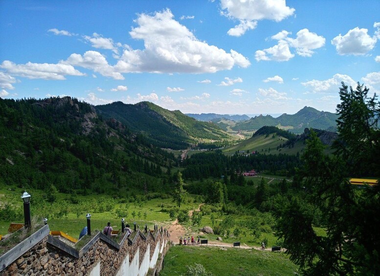 Un paisaje montañoso con un valle, un muro de piedra y personas caminando. 3
