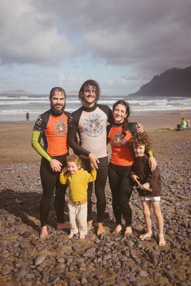 Une famille se trouve sur une plage rocheuse, avec l’océan et ses vagues en arrière-plan. 5