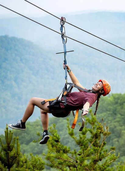 Una persona che fa zip-line con imbracatura e casco, sospesa tra i cavi sullo sfondo di montagne. 4